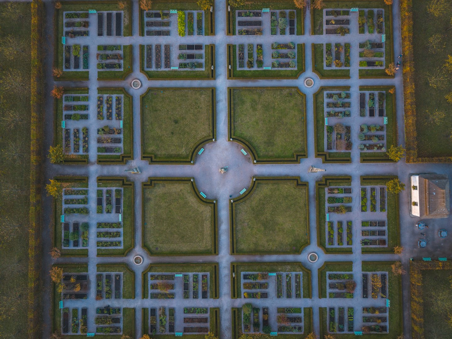 Giardino formale simmetrico con siepi curate e sentieri in pietra grigia.