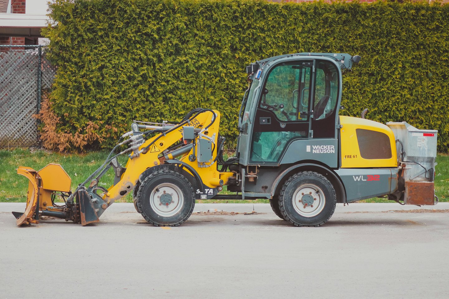 Spazzaneve giallo e grigio parcheggiato vicino a una siepe verde.